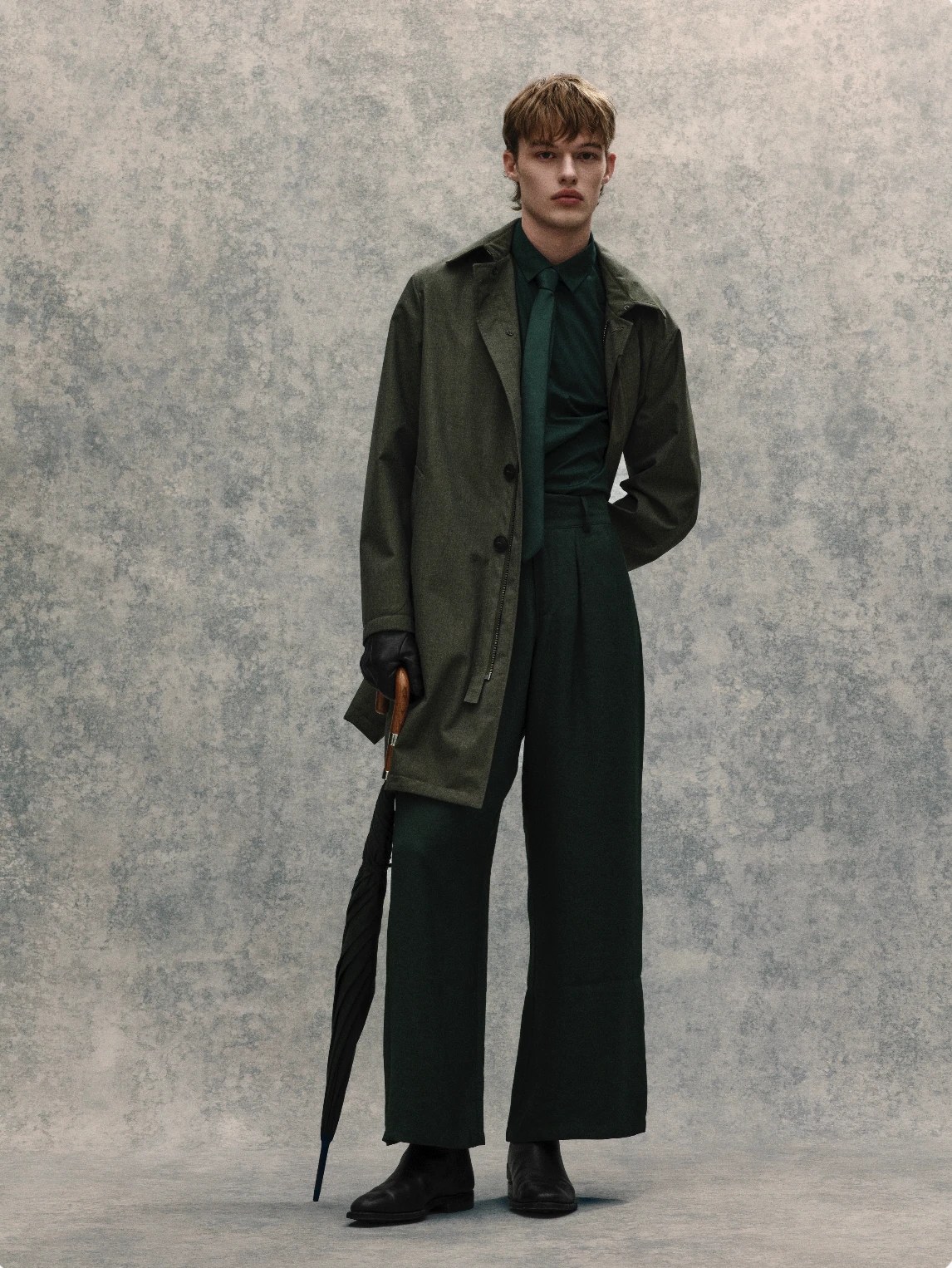Gordon Stabbins menswear shot: green overcoat, wide trousers and umbrella on a mottled backdrop